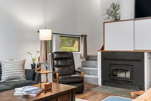 A living room with a sofa, a wooden coffee table, a leather chair, a fireplace, and a window with curtains. - Mad River Valley Modern 3 bedroom & 2 bath Condo; Convenient Location (Warren)