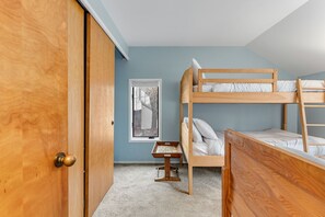 Een kamer met een stapelbed, een houten deur, een klein tafeltje en een raam.