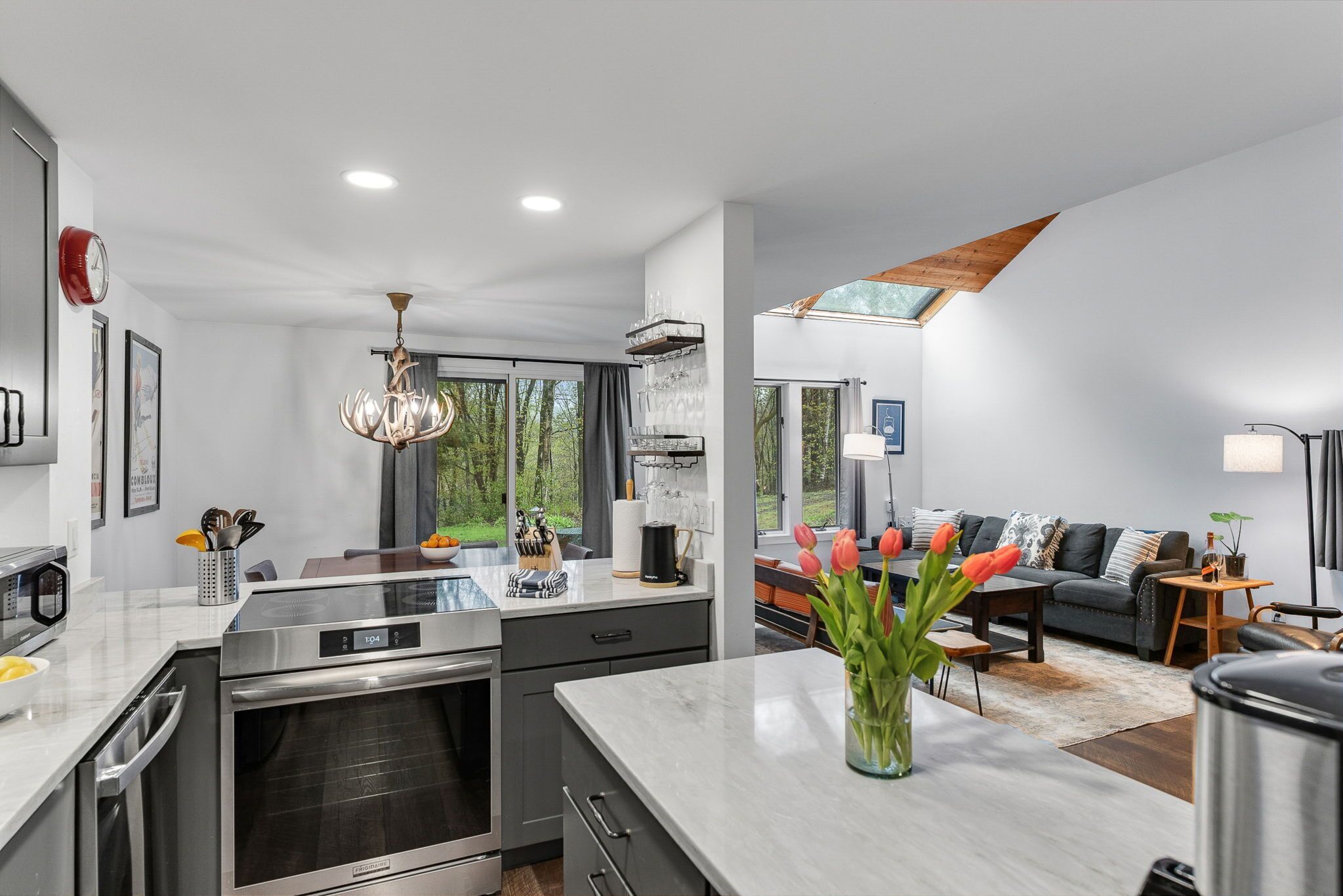 A modern kitchen with stainless steel appliances, a dining area with a sofa and tulips, and a large window providing natural light.