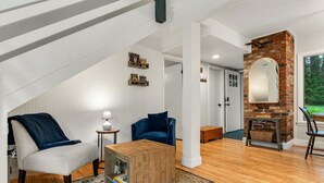 A loft-style room with a high ceiling, exposed beams, a brick fireplace, and a large mirror. - The Warren Nook: Your cozy, modern mountain basecamp. (Warren)