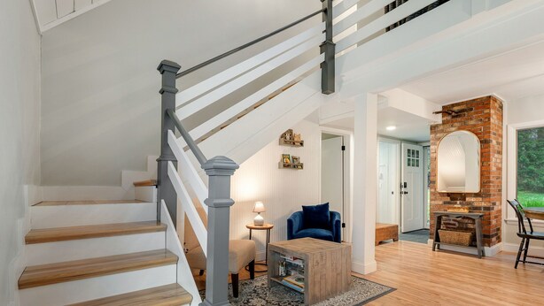 A staircase with wooden steps and a gray railing, a blue chair, a small wooden coffee table, and a brick fireplace. - The Warren Nook: Your cozy, modern mountain basecamp. (Warren)