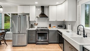 A modern kitchen with stainless steel appliances, white cabinetry, and a hexagonal tile backsplash. - The Warren Nook: Your cozy, modern mountain basecamp. (Warren)