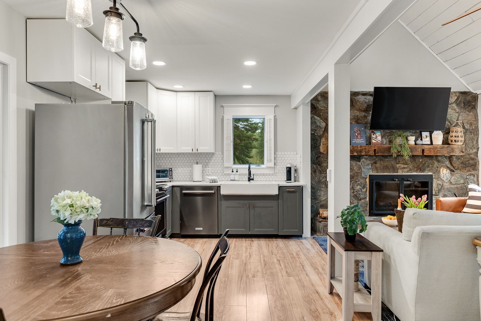A modern kitchen with a dining area, a stone fireplace, and a mounted television.