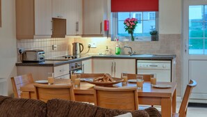 Eine moderne Küche mit Holzausstattung, einem eingebauten Backofen und einer Essecke mit Tisch für zwei Personen.