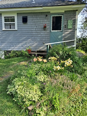 Ein Haus mit Veranda, einem kleinen Garten mit Blumen und einem Briefkasten.