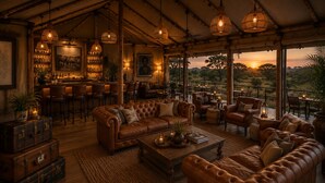 Un rincón de descanso acogedor con sofás de cuero, un bar con botellas y vistas a la puesta de sol.