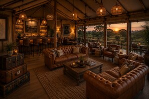 A cozy lounge area with leather sofas, a bar with bottles, and a view of the sunset.