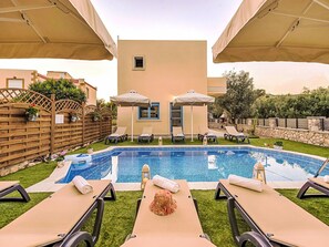 Un espace piscine équipé de chaises longues, de parasols et d’un petit bâtiment doté d’une fenêtre.