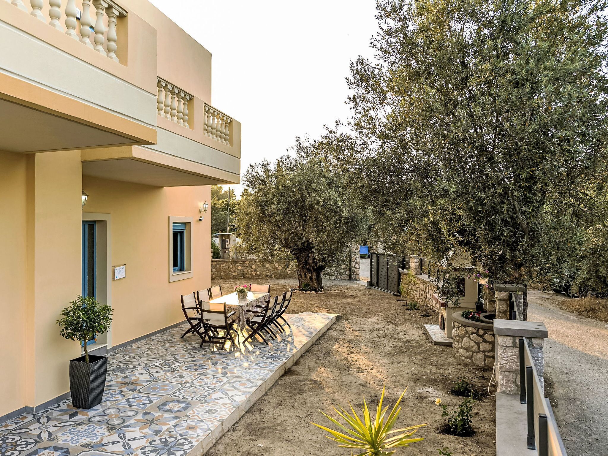 A courtyard with a tiled patio, outdoor seating, a stone wall, and a tree.