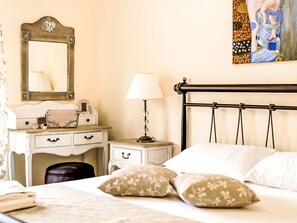 A bedroom with a bed, pillows, a nightstand, a lamp, a dresser, a mirror, and a painting on the wall. - Retro Villas - Superior with Pool by Interhome (Pefki)