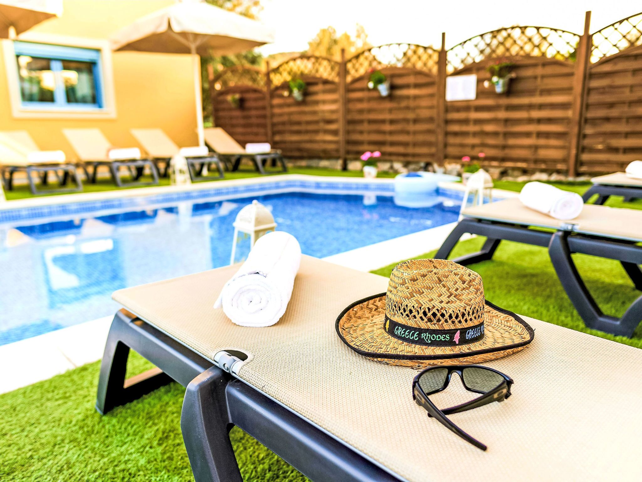 Un espace aménagé au bord de la piscine, avec des chaises longues, une piscine et une clôture en bois.