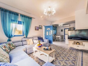 A living room with a sofa, coffee table, and TV. There is a dining area with chairs and a table. - Retro Villas - Deluxe with Pool by Interhome (Pefki)