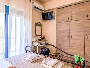 A bedroom with a bed, a TV mounted on the wall, a wooden wardrobe, and a window with curtains. - Retro Villas - Deluxe with Pool by Interhome (Pefki)