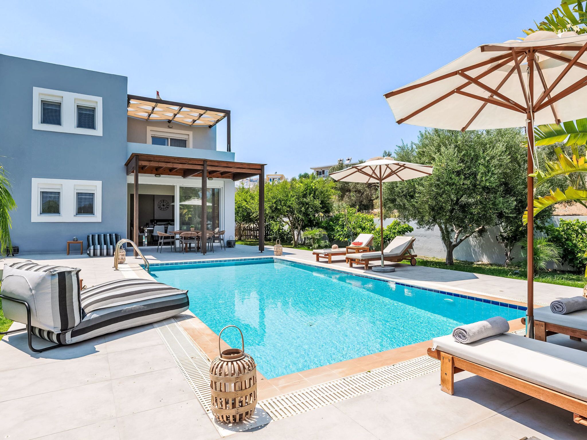 A swimming pool with lounge chairs and umbrellas, a covered patio area, and a modern house with large windows.