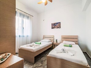 A hotel room with two wooden beds, a small table with a plate of food, a window with sheer curtains, and a painting on the wall. - Deep Blue by Interhome (Lachania)