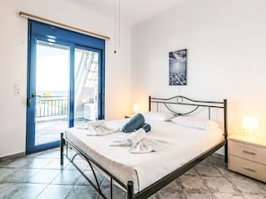 A bedroom with a bed, a nightstand, a lamp, a painting, and a sliding glass door leading to a balcony. - Deep Blue by Interhome (Lachania)