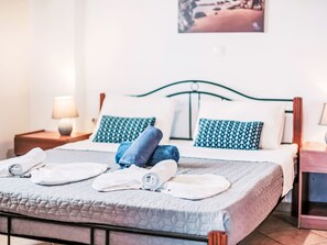 Uma cama bem arrumada com toalhas dobradas, um travesseiro estampado e uma cabeceira.