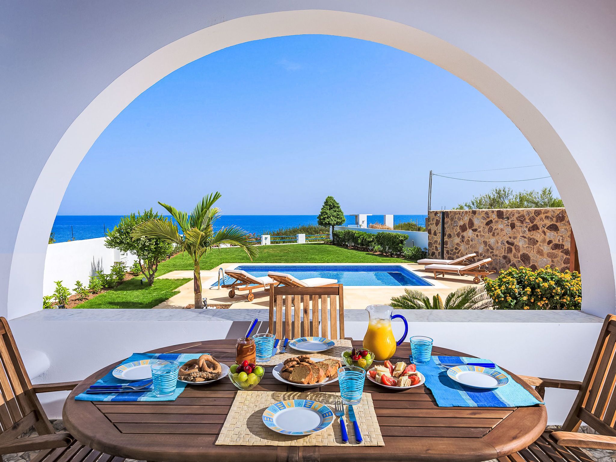 Taula de dinar amb articles per a l'esmorzar, una piscina i vista al mar.