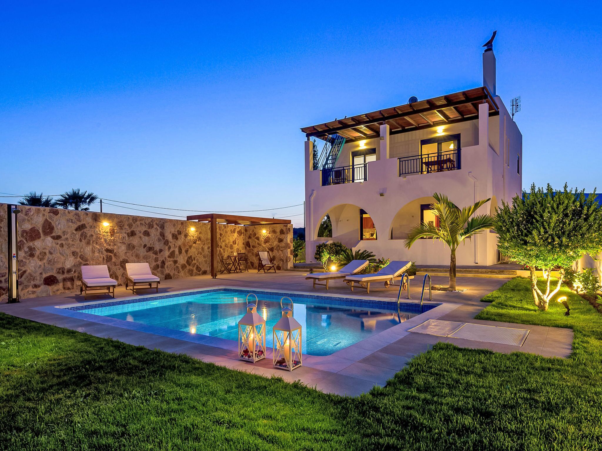 Una casa moderna de dos pisos con piscina, mobiliario exterior y una pared de piedra.