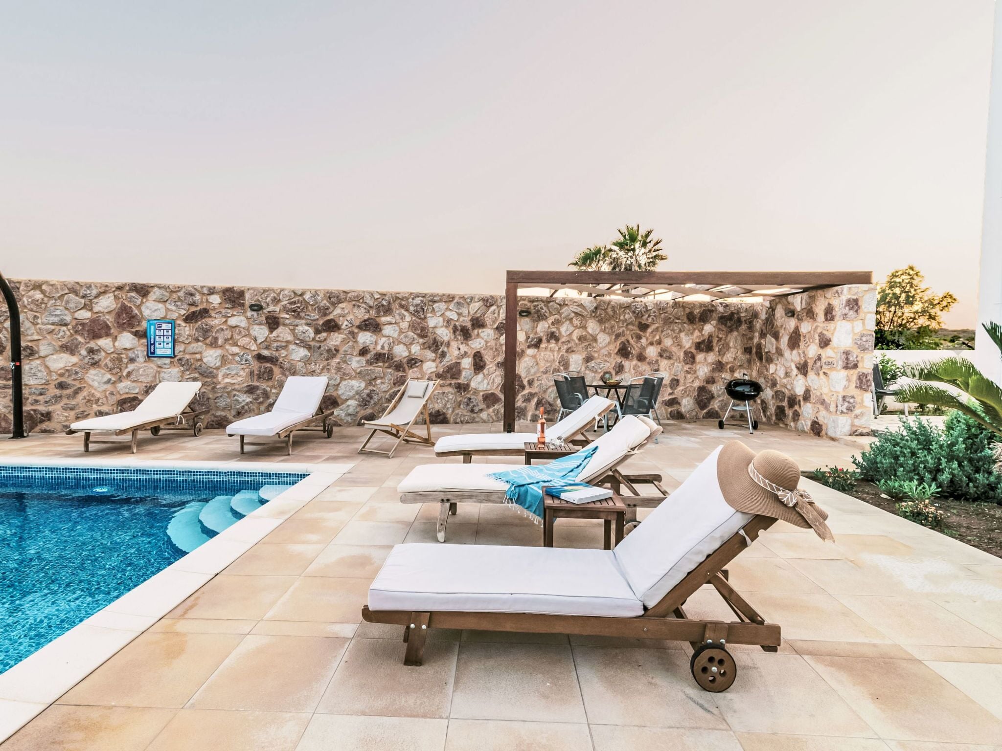 A poolside area with lounge chairs, a stone wall, and a pergola.