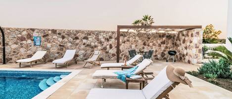 A poolside area with lounge chairs, a stone wall, and a pergola.