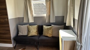 A room with a dark-colored sofa, two decorative pillows, a window with curtains, and a wooden floor. - RBR 1463  - Beach Resort Kamperland by Interhome (Kamperland)