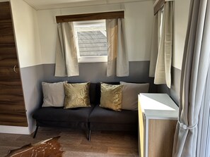 Ein Zimmer mit einer dunkelgrauen Couch, zwei Zierkissen, einem Fenster mit Vorhängen und einem Holzboden.