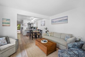 Ein modernes Wohnzimmer mit Sofa, Couchtisch und einem gemusterten Sessel. Im Hintergrund ist eine Essecke mit Stühlen und einem Tisch zu sehen.