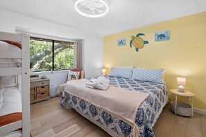 Ein Schlafzimmer mit Etagenbett, einem großen Bett mit gemusterten Textilien, einem Fenster mit Blick auf Bäume und Wandbildern.