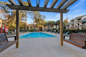 Un área de piscina con una pérgola de madera, sillones de descanso y una pileta.