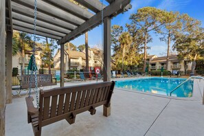 A wooden swing bench under a pergola, a swimming pool, and a poolside lounge area with sun loungers and umbrellas. - 
Coastal Retreat Steps from Coligny Beach, Dining, Shops, and Celebration Park! (Hilton Head Island)