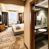 Ein Hotelzimmer mit Bett, Schreibtisch, Stuhl, Bad mit Waschbecken und Spiegel sowie Blick auf die Stadt.