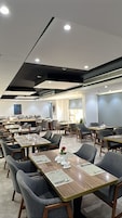 Un espace de restauration moderne dans un hôtel, avec de nombreuses tables et chaises, un éclairage encastré et une grande fenêtre.