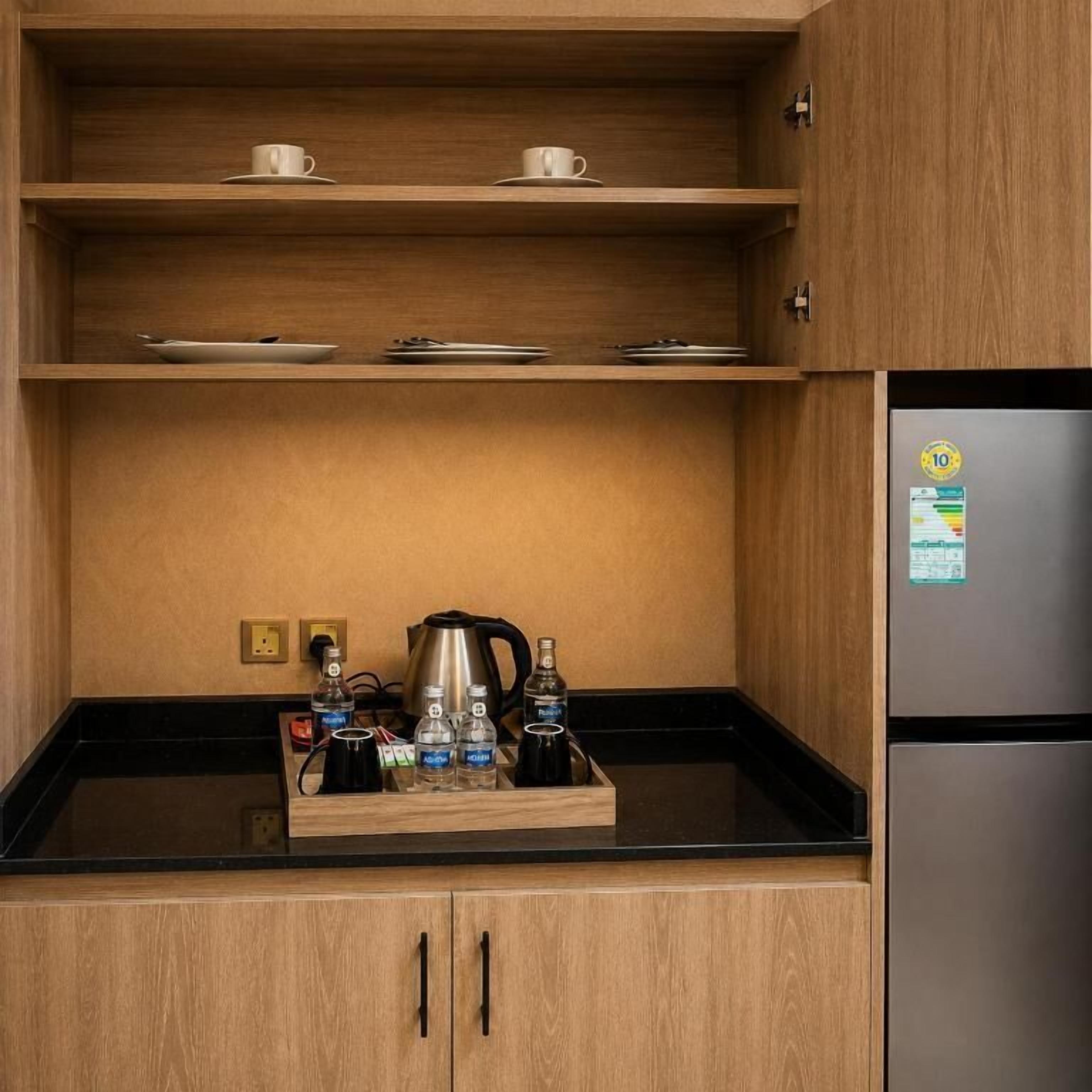 A compact kitchenette with wooden cabinets, a black countertop, and a stainless steel refrigerator.