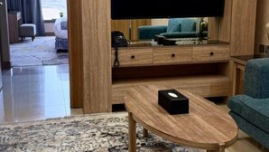 A modern living room with a flat-screen TV, wooden furniture, and a patterned rug. - Medhal Hotel (Jeddah)