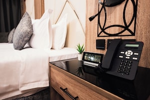 Habitación de hotel con una cama, una mesita de noche con un teléfono, un reloj pequeño y un cajón.