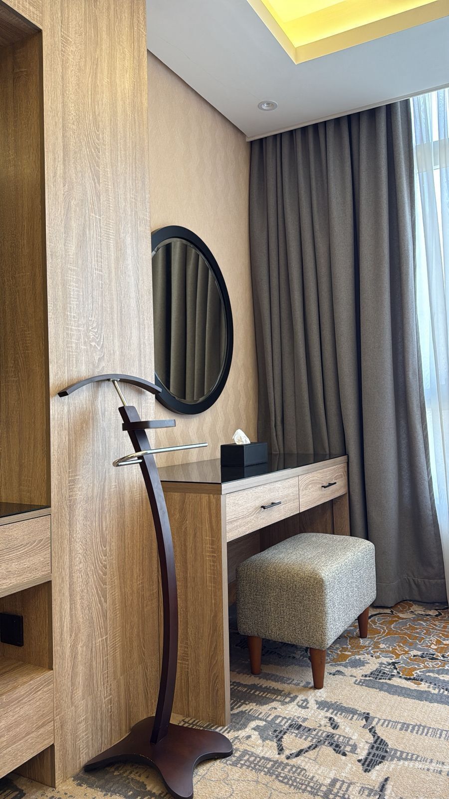 Une chambre d’hôtel avec une coiffeuse en bois, un miroir, un petit tabouret et un tapis à motifs.