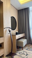 Habitación de hotel con tocador de madera, un espejo, un taburete pequeño y una alfombra estampada.