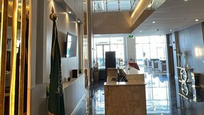 Un moderno vestíbulo de hotel con un mostrador de recepción, un ascensor de vidrio y un piso de mármol pulido.