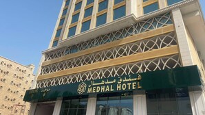 Un edificio de varios pisos con un letrero llamativo que dice 'MEDHAL HOTEL' y un letrero de estacionamiento debajo.