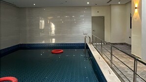 Una piscina interior con agua cristalina, escaleras de metal y anillos de seguridad rojos.