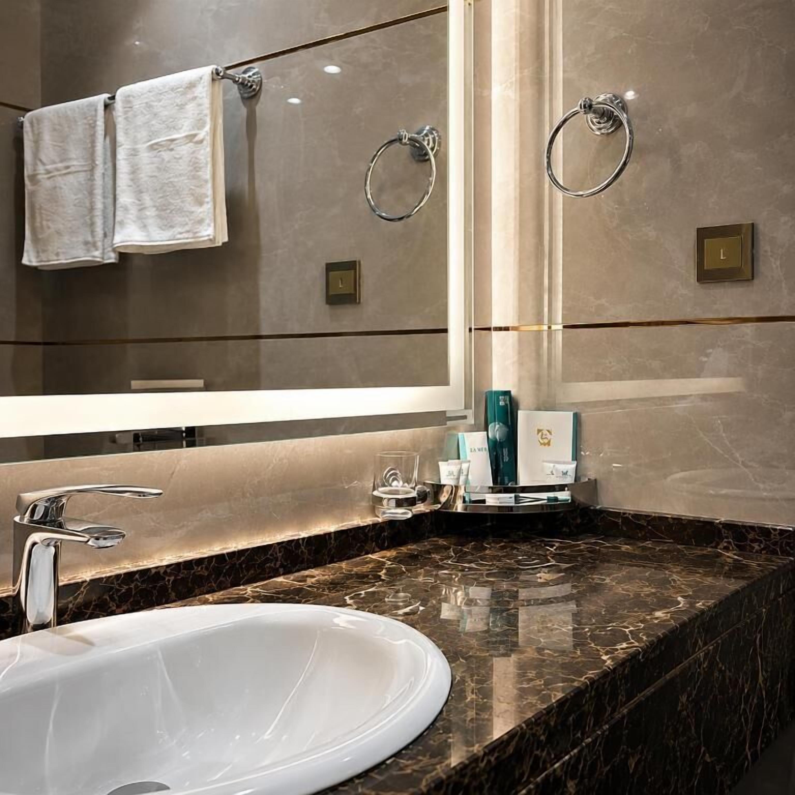 A modern bathroom with a large mirror, a white sink, and two towel rings.