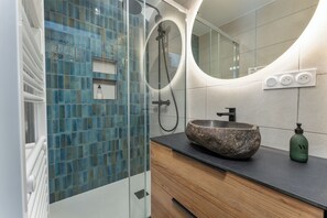 Ein modernes Badezimmer mit einer Duschkabine aus Glas, einem Steinsink und einem Holzwaschtisch.