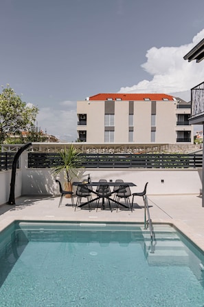 Ein Pool mit Tisch und Stühlen, ein Blumentopf und im Hintergrund ein Gebäude mit rotem Dach.