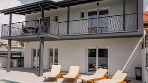 En modern byggnad i två våningar med en balkong, utomhusmöbler och en swimmingpool.