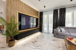 Ein modernes Wohnzimmer mit Fernseher, grauem Sofa, Couchtisch mit Snacks und einer Zimmerpflanze.
