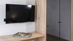 Ett modernt rum med ett skrivbord i trä, en svart stol, en platt-TV och en garderob med spegeldörrar.