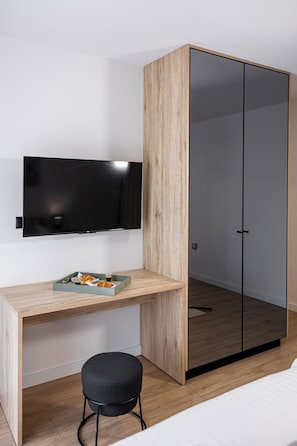 Ein modernes Zimmer mit Schreibtisch aus Holz, einem schwarzen Stuhl, einem Flachbildfernseher und einem Kleiderschrank mit Spiegeln.