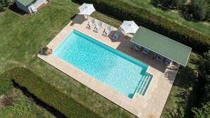 Eine Vogelperspektive zeigt einen rechteckigen Pool mit Fliesen umgeben von einem gepflegten Rasen und Hecken.