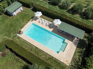 Eine Vogelperspektive zeigt einen rechteckigen Pool mit Fliesen umgeben von einem gepflegten Rasen und Hecken.